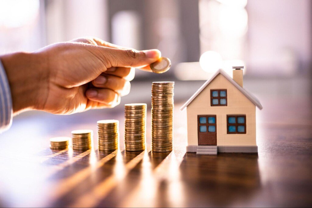 pilha de moedas ao lado de casa em miniatura, representando a compra de apartamentos na planta