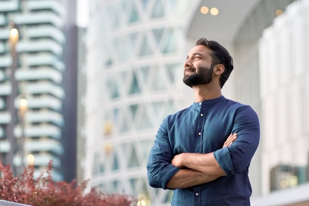 Homem de camisa azul olhando para o céu em volta de prédios