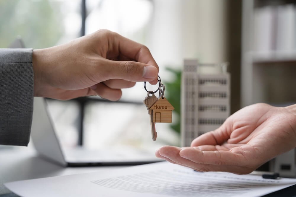 A mão de um homem entregando a chave de uma casa para outro homem