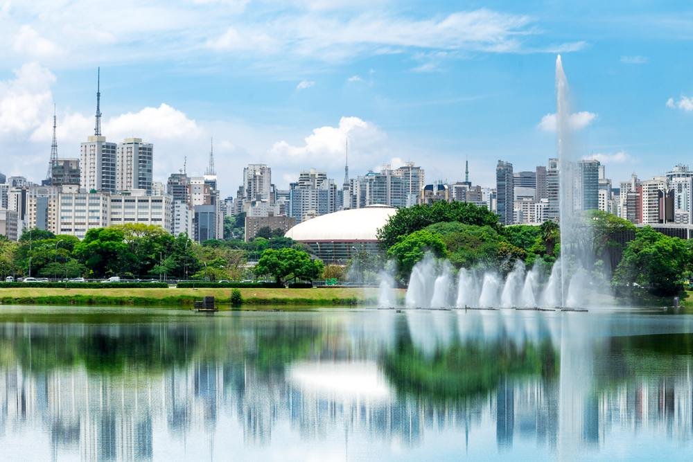 Um lago, com uma cidade a frente, árvores e prédios atra´s