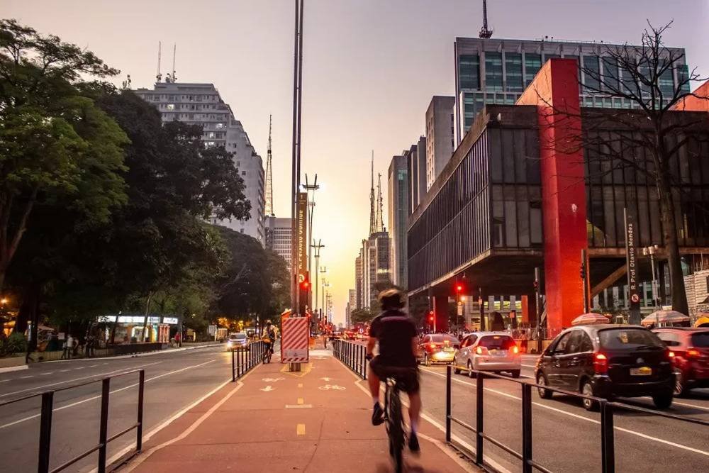 homem andando de bicicleta em uma ciclovia em uma cidade com carros e prédios