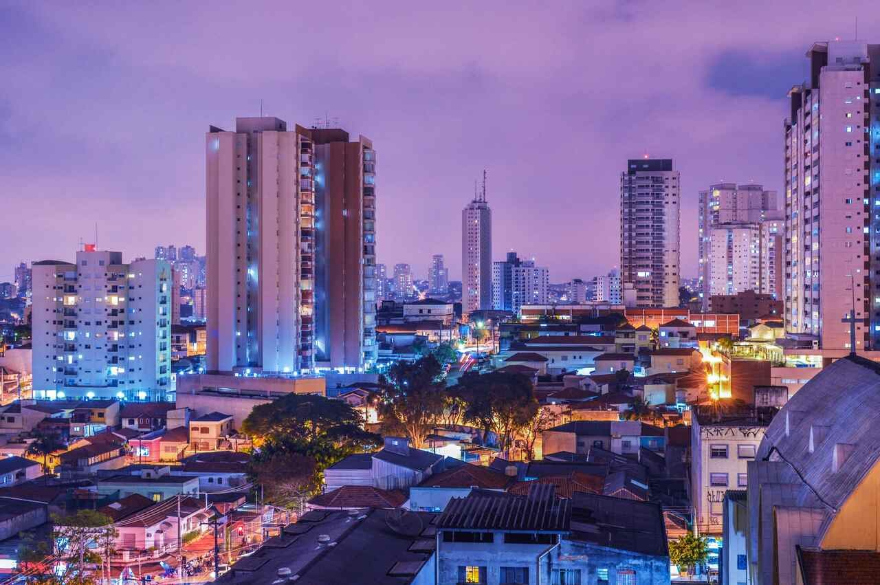 Avenida movimentada em São Paulo ao entardecer, cercada por prédios altos.