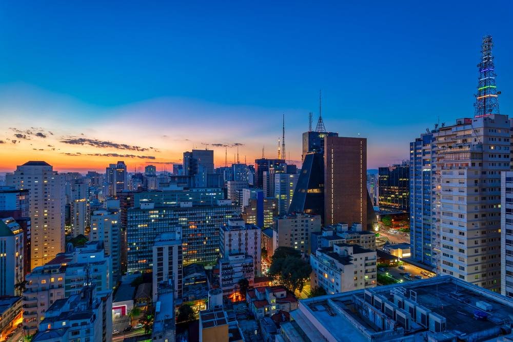 Vista panorâmica do skyline urbano de São Paulo ao entardecer, com prédios modernos e céu azul claro